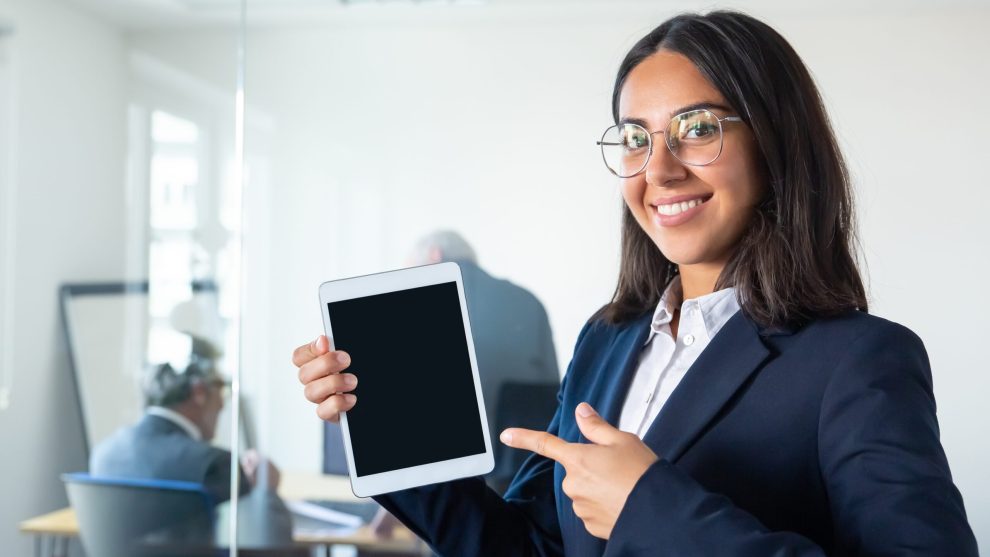 Happy confident business lady holding tablet Happy confident business lady holding tablet, showing and pointing finger at blank screen, looking at camera and smiling. Copy space. Communication and advertising concept